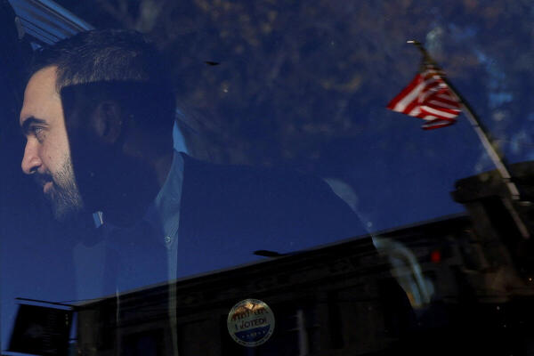 A US flag is reflected in the door as Democratic candidate for New York City mayor, Zohran Mamdani, stands at a car after casting his vote in the New York City mayoral election, outside a polling site at the Frank Sinatra School of the Arts High School in Astoria, Queens borough of New York City, US.