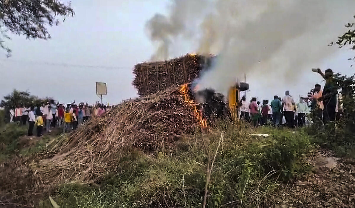 People look on as smoke billows from sugarcane on fire after several tractors and trolleys carrying sugarcane to a factory were allegedly set ablaze by miscreants, in Bagalkote district, Karnataka