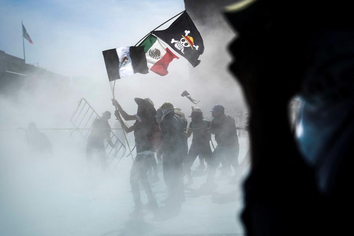 Demonstrators carry a Mexican flag, a black and white version of a Mexican flag and a One Piece flag as riot control agents are sprayed on them during a protest against insecurity and corruption in the country, on Mexico City, Mexico.