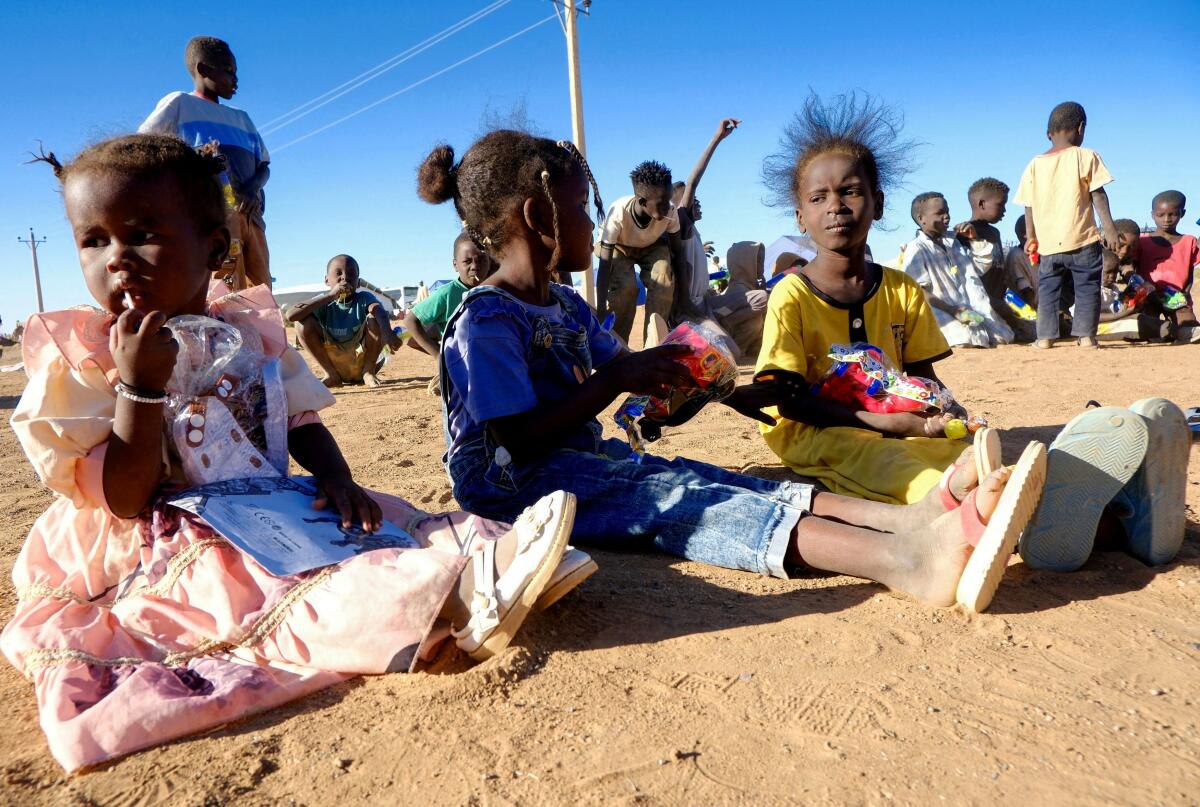 Displaced girls from El Fasher sit on the ground with toys in their hands, in a displacement camp in Al-Dabbah, Sudan.