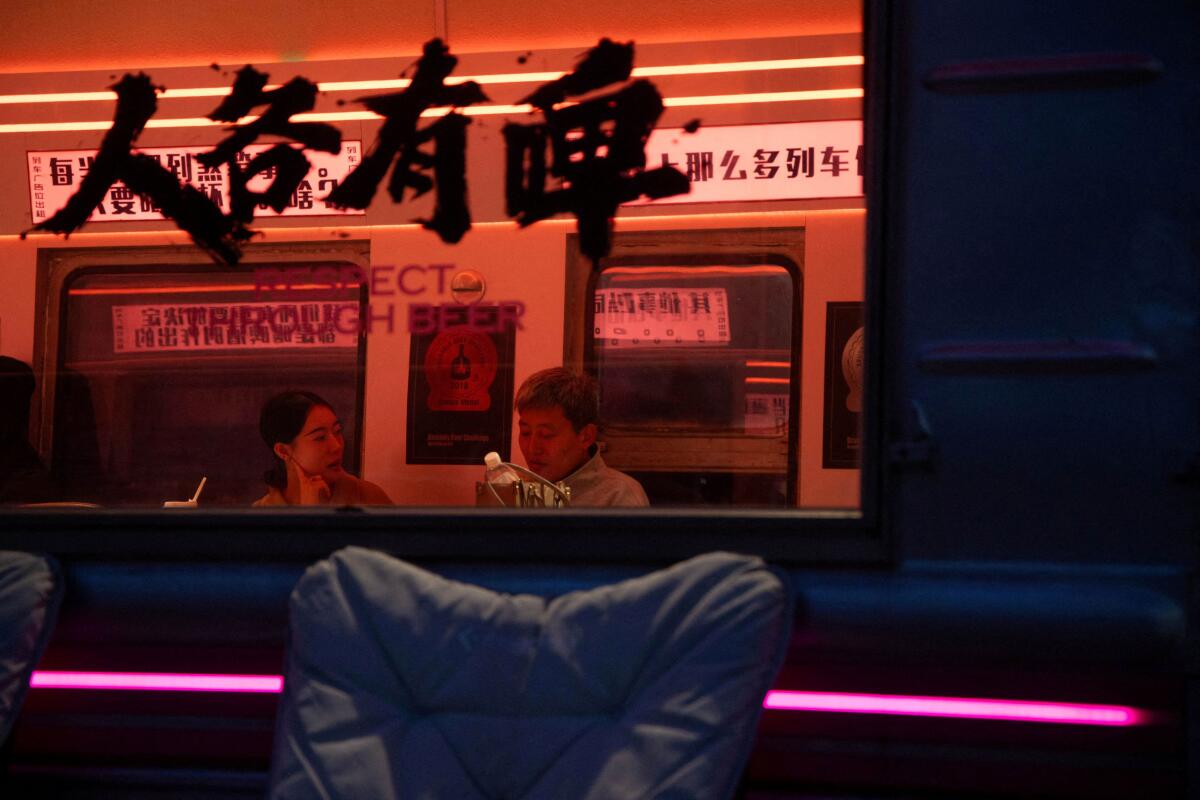 A couple talk inside a railway carriage transformed into a bar at the 798 Art District in Beijing, China, November 23, 2025.
