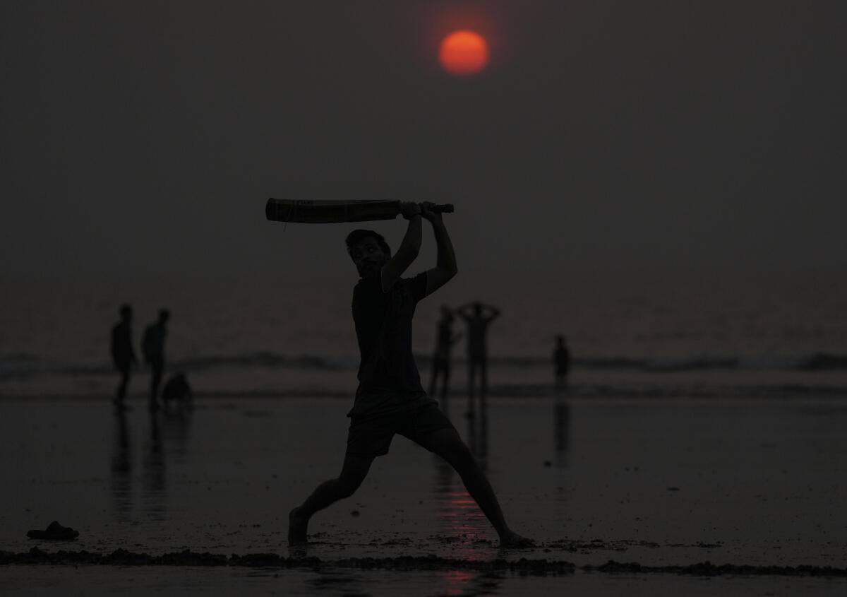 A boy playing cricket is silhouetted against the setting sun on a beach, in Mumbai, Maharashtra, Sunday, Nov. 23, 2025.