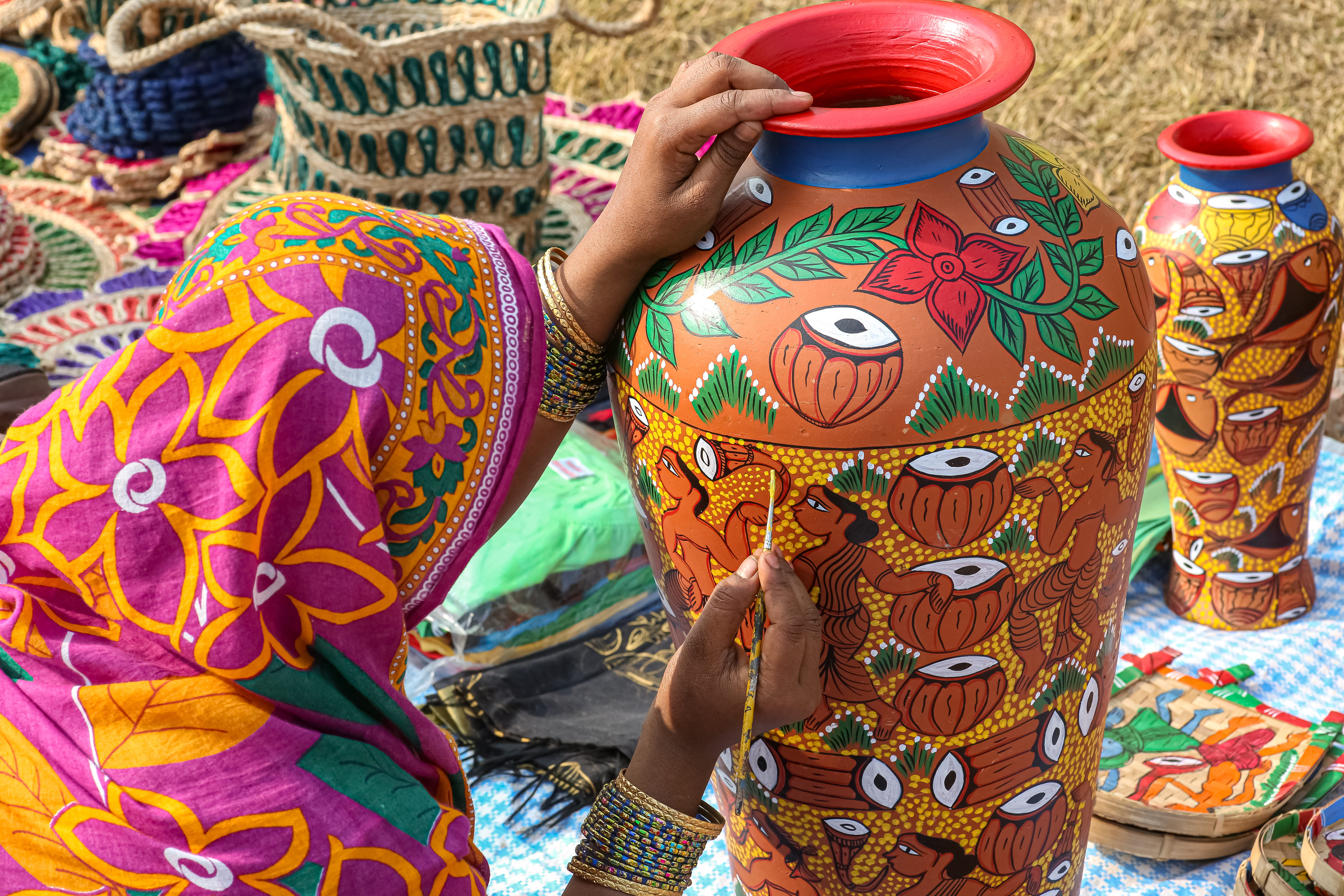 Rural Indian woman wearing traditional costume painting a clay handmade vase at handicraft fair at Kolkata