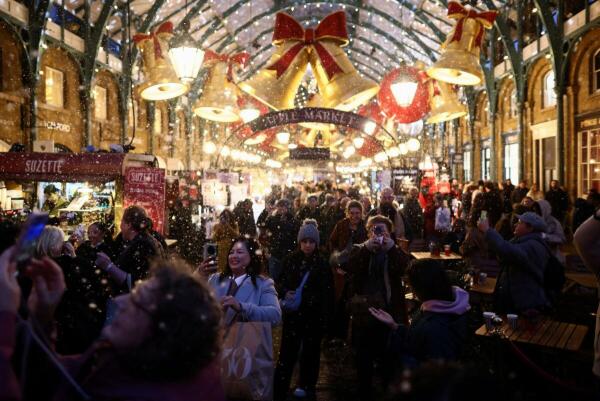 People walk through a christmas market in Covent Garden as artificial snow falls in London, Britain