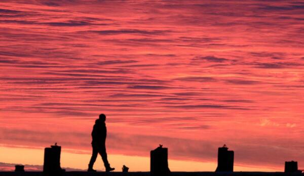 A fisherman walks on a pier over calm waters of the Black Sea at sunset off the coast of Yevpatoriya, Crimea.