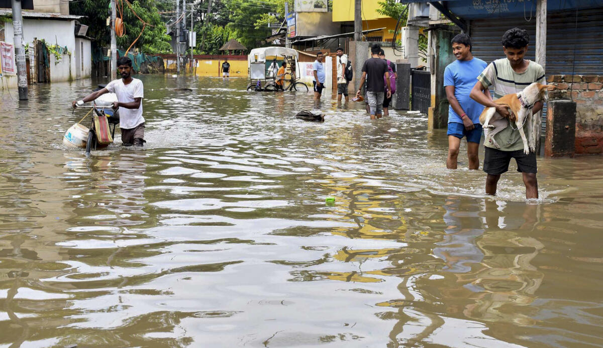 Commuters make their way through a waterlogged road after rainfall.