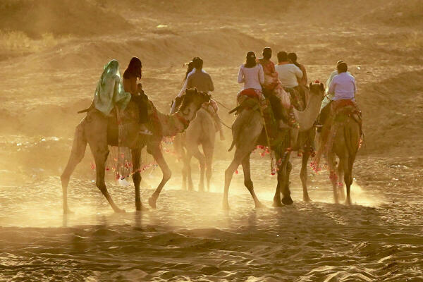 People take a camel ride across sandy terrain, in Pushkar, Ajmer.