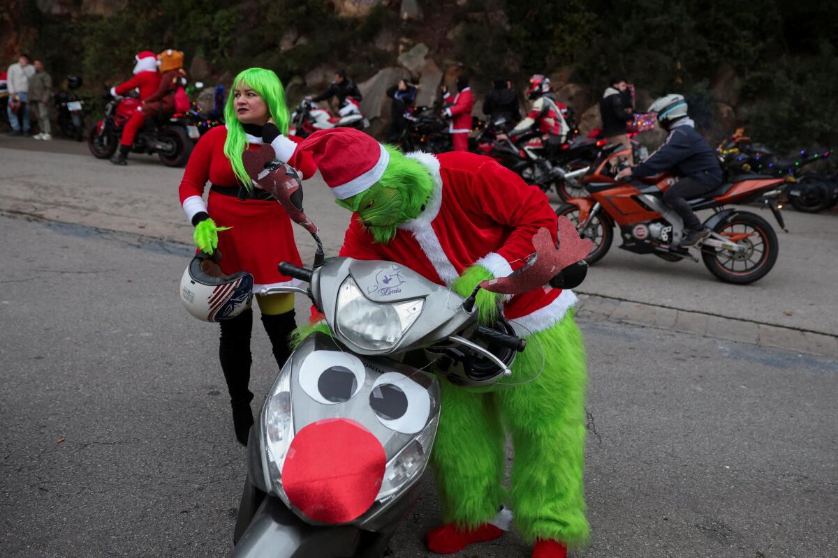 A person d.ressed as the Grinch prepares a decorated scooter to participate in a Santa-themed motorcycleride in Barcelona, Spain.