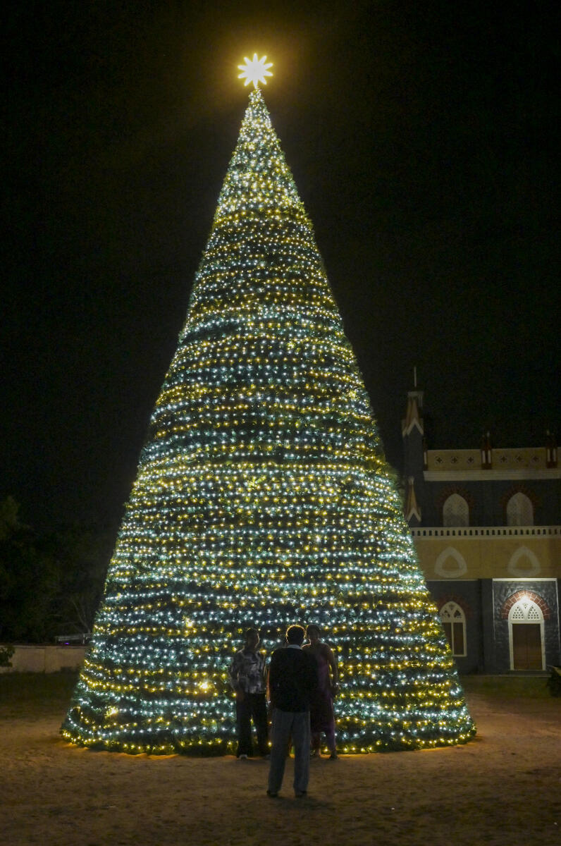 People pose near an illuminated Christmas tree on display at St. Ignatius of Loyola Roman Catholic Church, Puthenthope, ahead of Christmas and New Year celebrations, in Thiruvananthapuram.