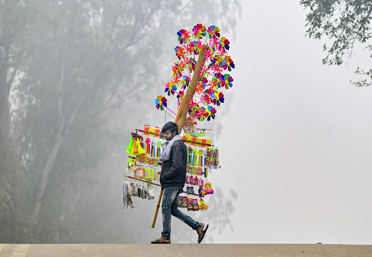 A toy vendor walks on a road on a foggy winter morning, in Prayagraj, Tuesday, Dec. 30, 2025. 