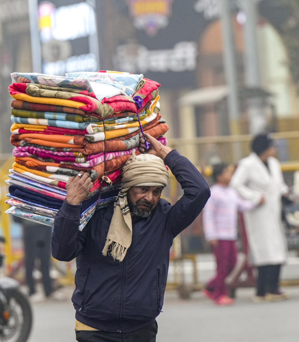 A street vendor carries a stack of blankets for sale amid winter chill, in Lucknow, Friday, Jan. 2, 2026.