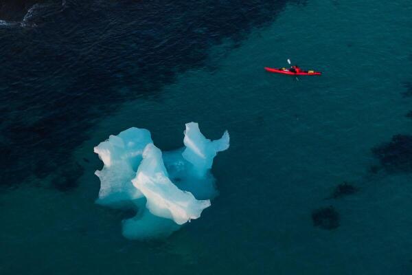 A drone view a man kayaking next to an iceberg in Nuuk, Greenland.
