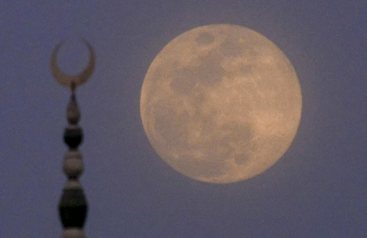 A full moon is seen in the evening sky with the crescent finial of a mosque in the foreground, in Patna.