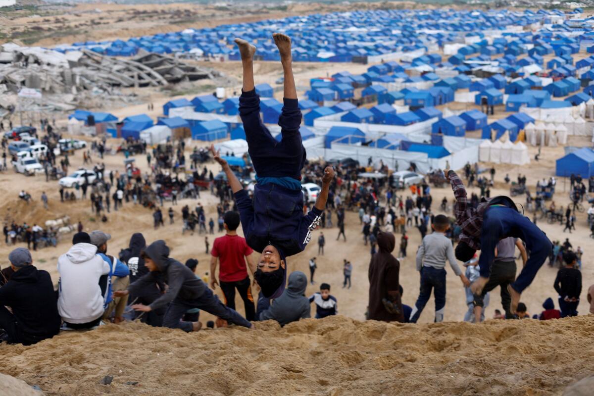 A Palestinian youth jumps as Palestinian youths perform stunts with motorbikes near displaced persons' tents in the central Gaza Strip, February 6, 2026.