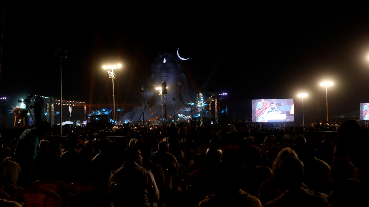 Group of people gather together during mahashivratri festival celebration event at night in front of Aadiyogi Lord Shiva 112 feet tall statue.