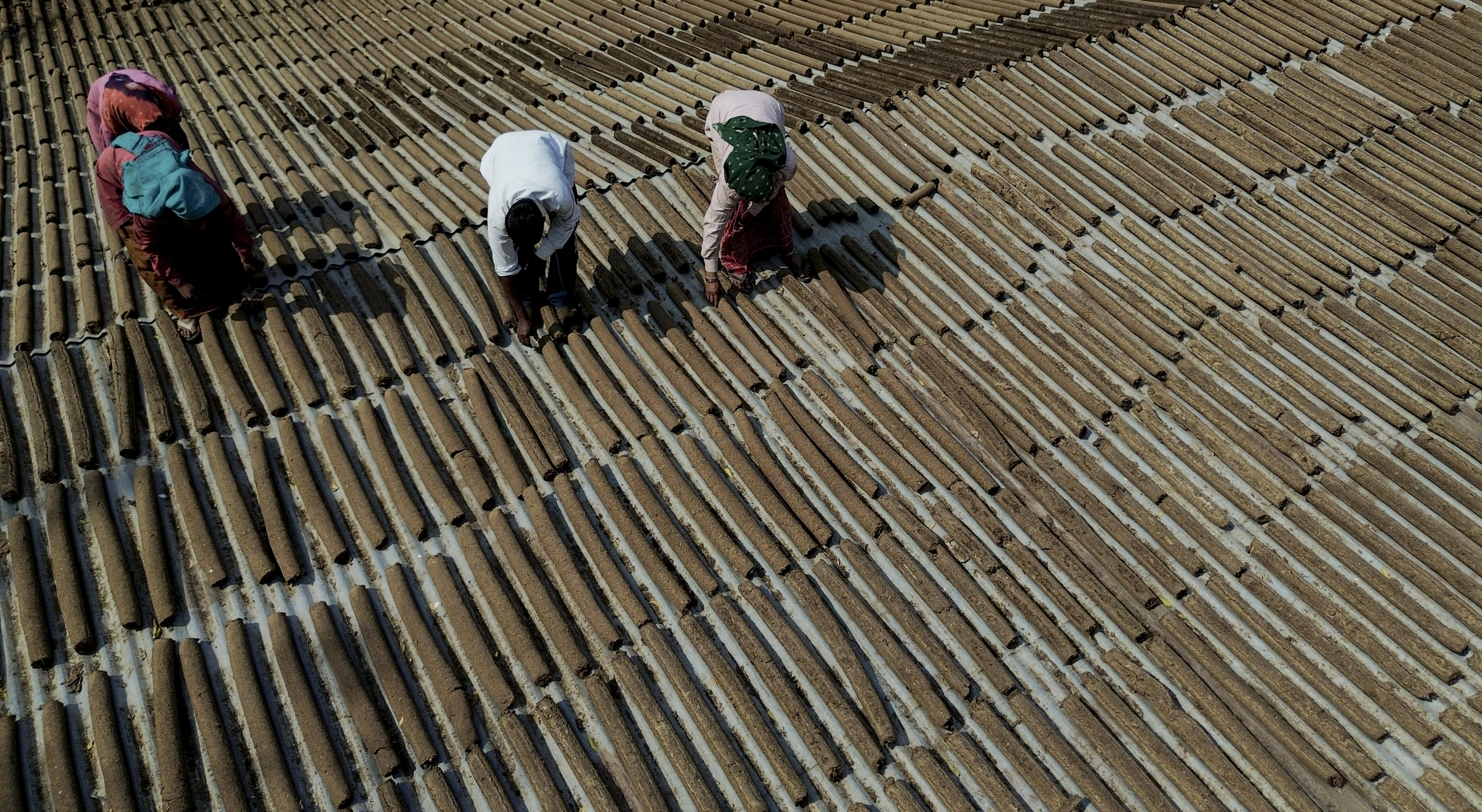 Workers place logs made of cow dung, used to light a bonfire, atop a tin shed