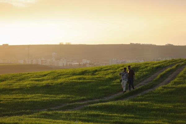 People walk outdoors, with the city of Cizre visible in the background, following a long atmospheric depression, near the Syrian-Turkish border in Derik, Syria.