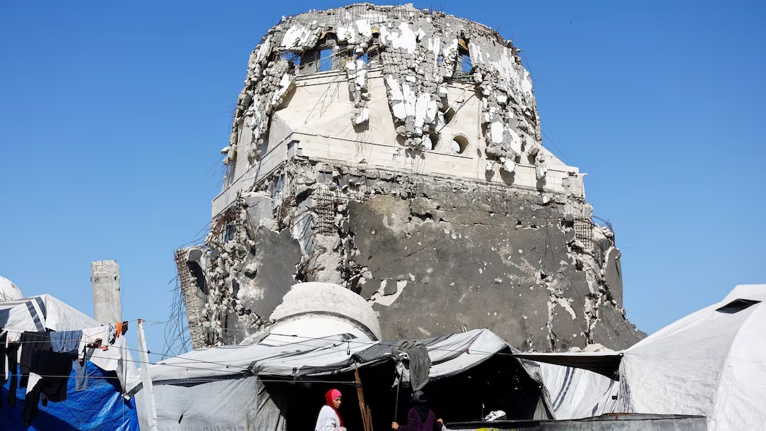 Displaced Palestinian women stand at a tent camp surrounding a mosque.