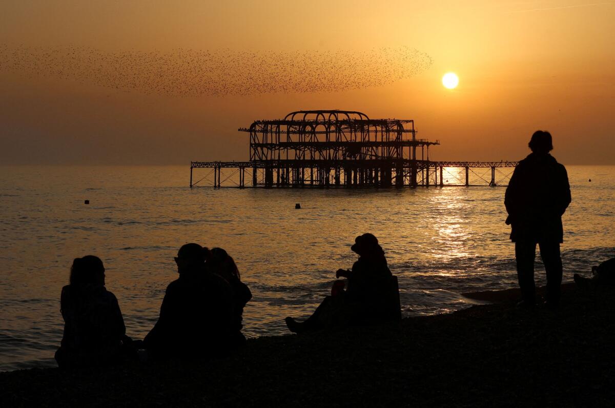 People enjoy warm weather at sunset as a murmuration of starlings fly above the West Pier in Brighton, Britain.