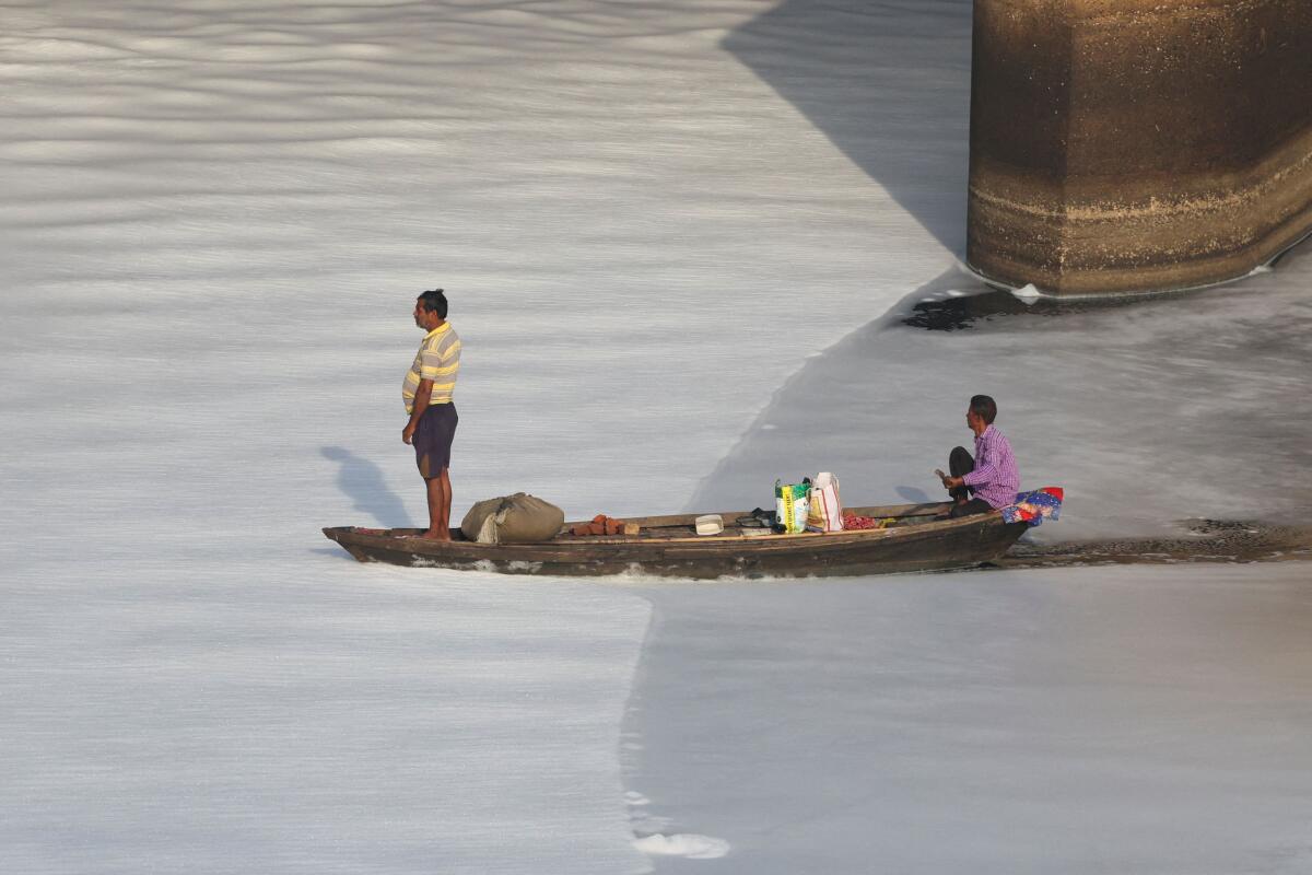 Fishermen ride a boat through foam on the polluted Yamuna river, in New Delhi