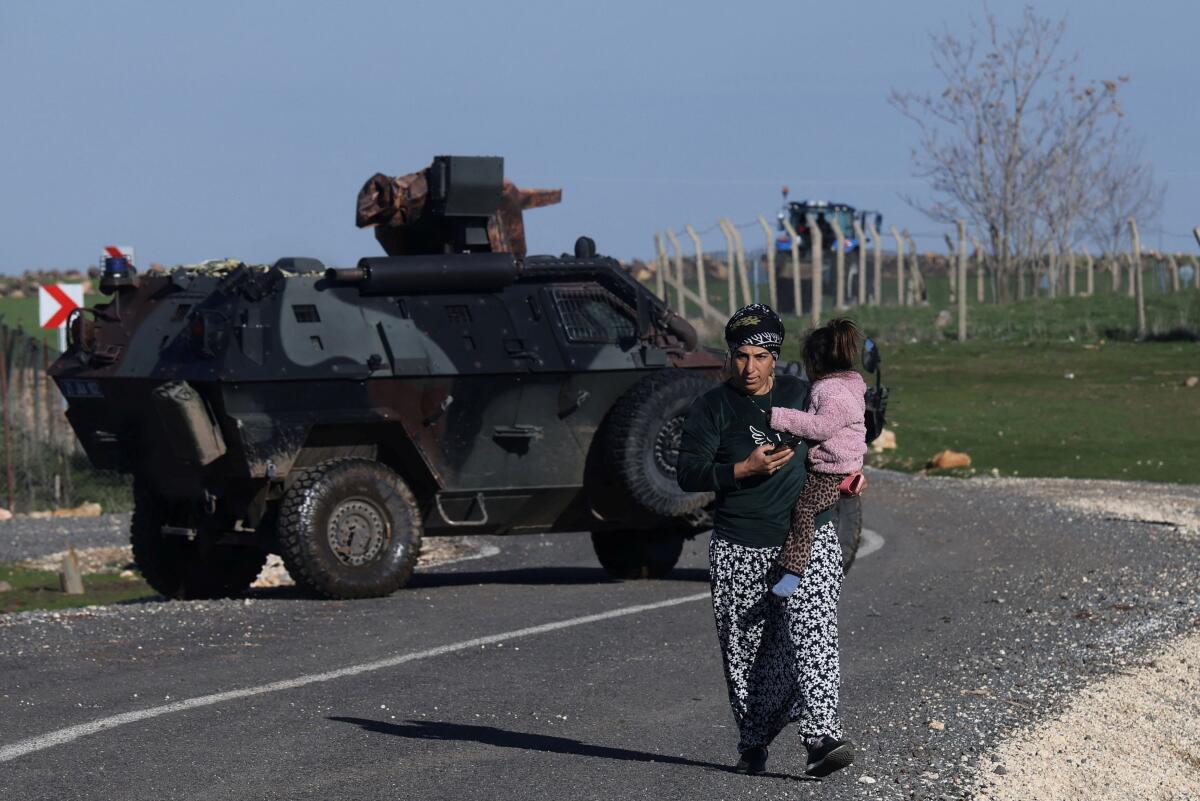 A woman carrying a child walks past an armoured vehicle as Turkish army and security personnel search a field after a piece of ammunition fell following the interception of a missile launched from Iran by a NATO air defence system, in Diyarbakir, Turkey.