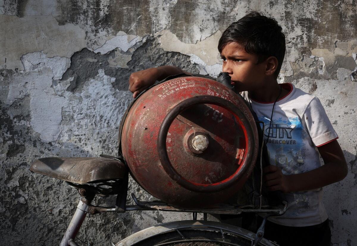 A boy stands next to an empty LPG cylinder outside a gas agency in Noida.