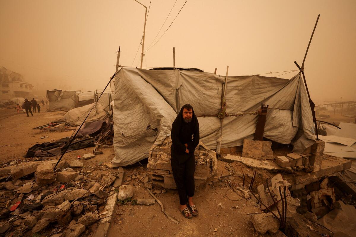 A man stands next to a tent as Palestinians displaced during the two-year Israeli offensive shelter in a tent camp, during a sandstorm in Gaza City, March 14, 2026. 