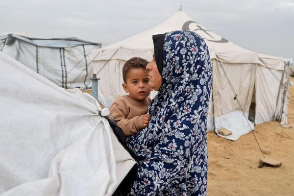 A woman holds a child, as displaced Palestinians shelter in a tent camp on a windy day in Khan Younis in the southern Gaza Strip.