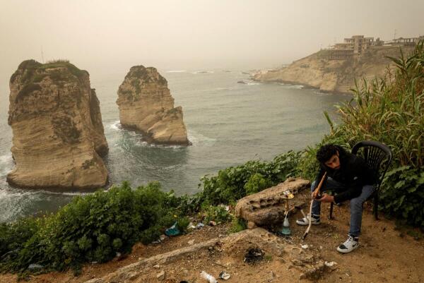 A man smokes shisha next to the Raouche Rocks, as dust covers the city, amid escalating hostilities between Israel and Hezbollah, as the U.S.-Israel conflict with Iran continues, in Beirut, Lebanon.