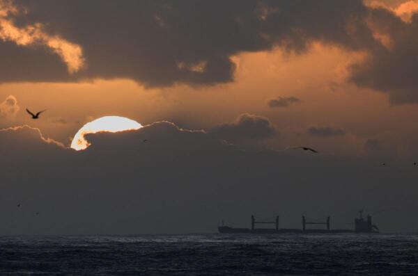 A ship moves through the water during sunset at Green Point, near the harbor, in Cape Town, South Africa.