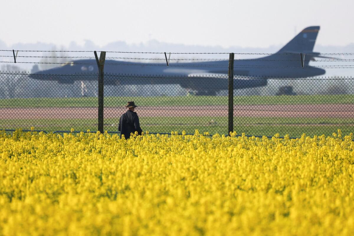A person standing in a rape field sees a US Air Force B‑1B Lancer military aircraft parked at RAF Fairford Air Force Base.