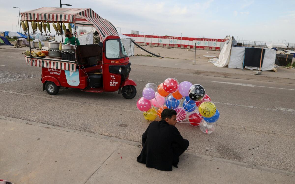 A displaced boy sells balloons as another displaced vendor sells food at a makeshift encampment, amid a temporary ceasefire between Lebanon and Israel, in Beirut.
