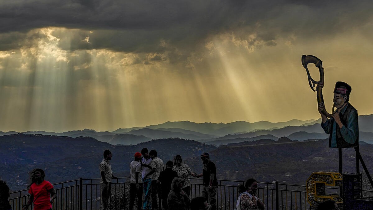 People gather at a viewpoint as clouds hover and sun rays pierce through them, in Shimla, Himachal Pradesh, Sunday, May 3, 2026.