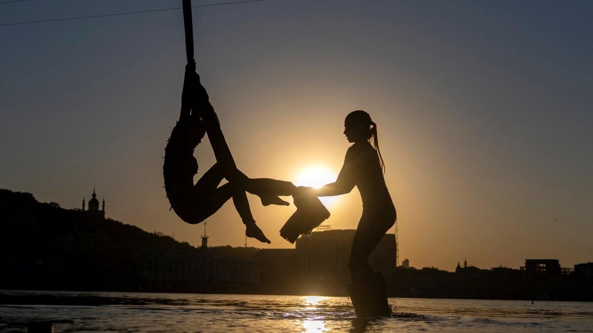 Women practice aerial acrobatics on aerial silks suspended from a bridge over the Dnipro River amid Russia's attack on Ukraine at sunset on a hot spring day in Kiev, Ukraine, May 6, 2026.