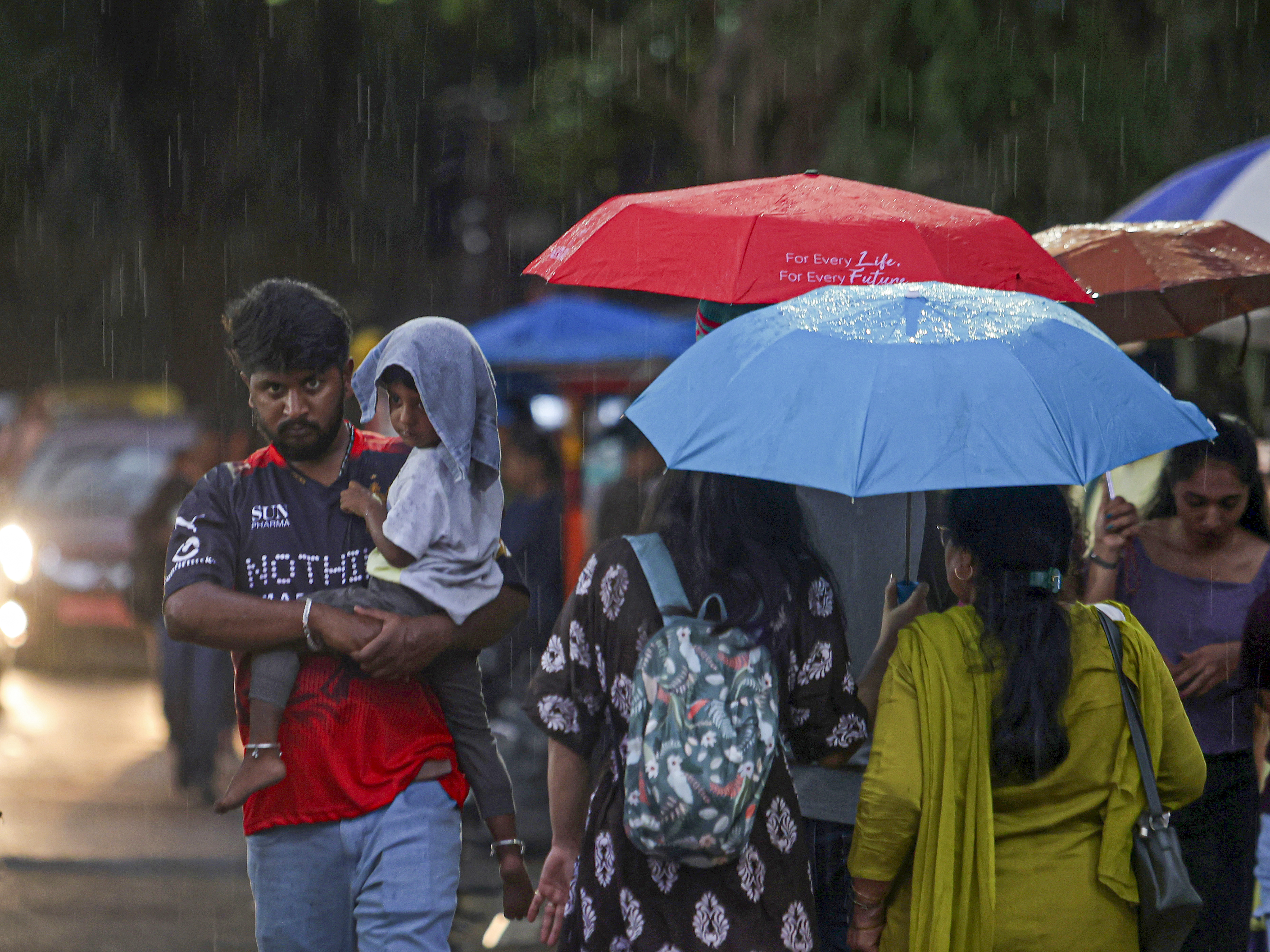 A man covers a kid during rain, in Bengaluru, Karnataka