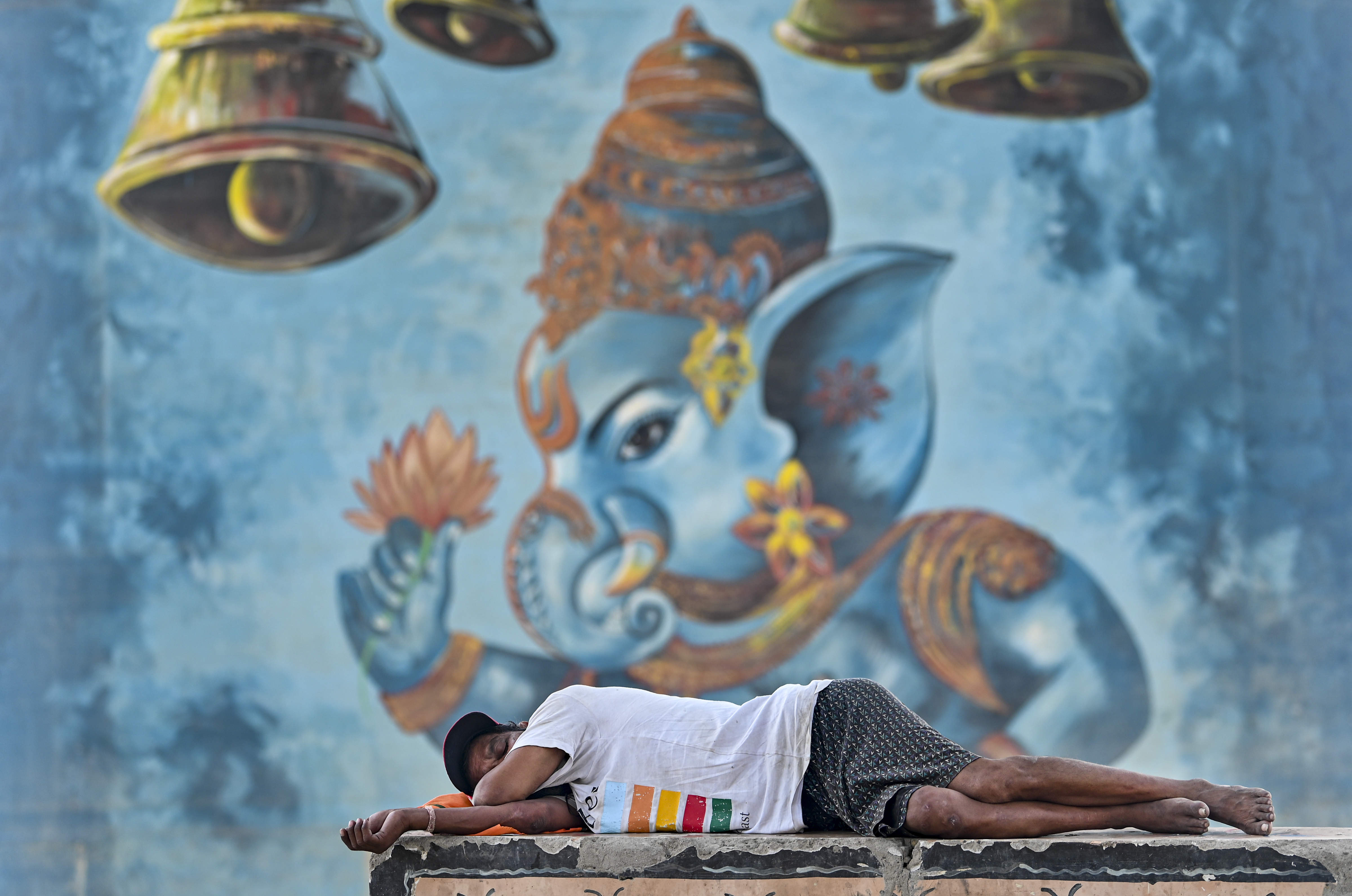 A man rests under a railway bridge over the River Ganga on a hot summer day