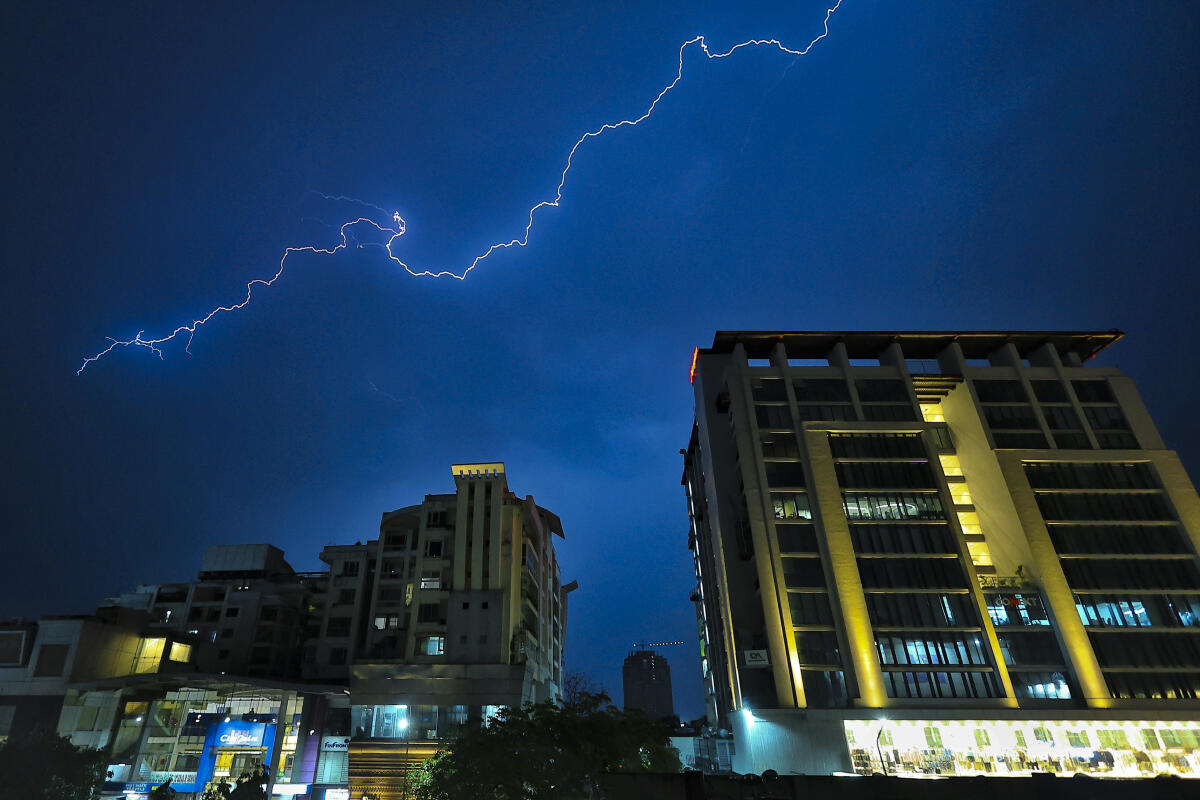 Lightning streaks across the sky over buildings during rain and thunderstorm, in Jaipur.