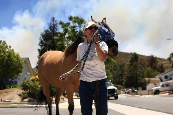 A woman reacts while she guides a horse as smoke rises from a wildfire known as the Sandy Fire