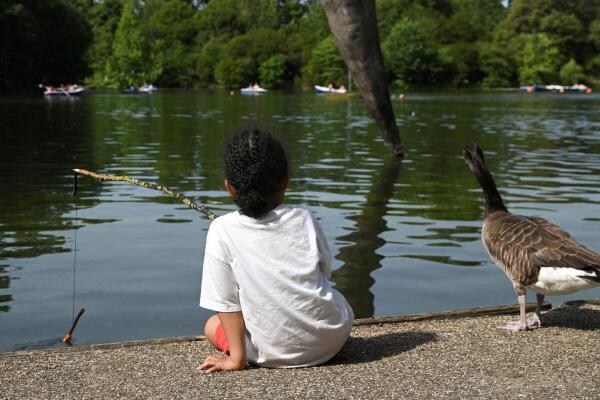 A boy fishes with a stick as a duck sits next to him, at Victoria Park in Hackney, in London, Britain.