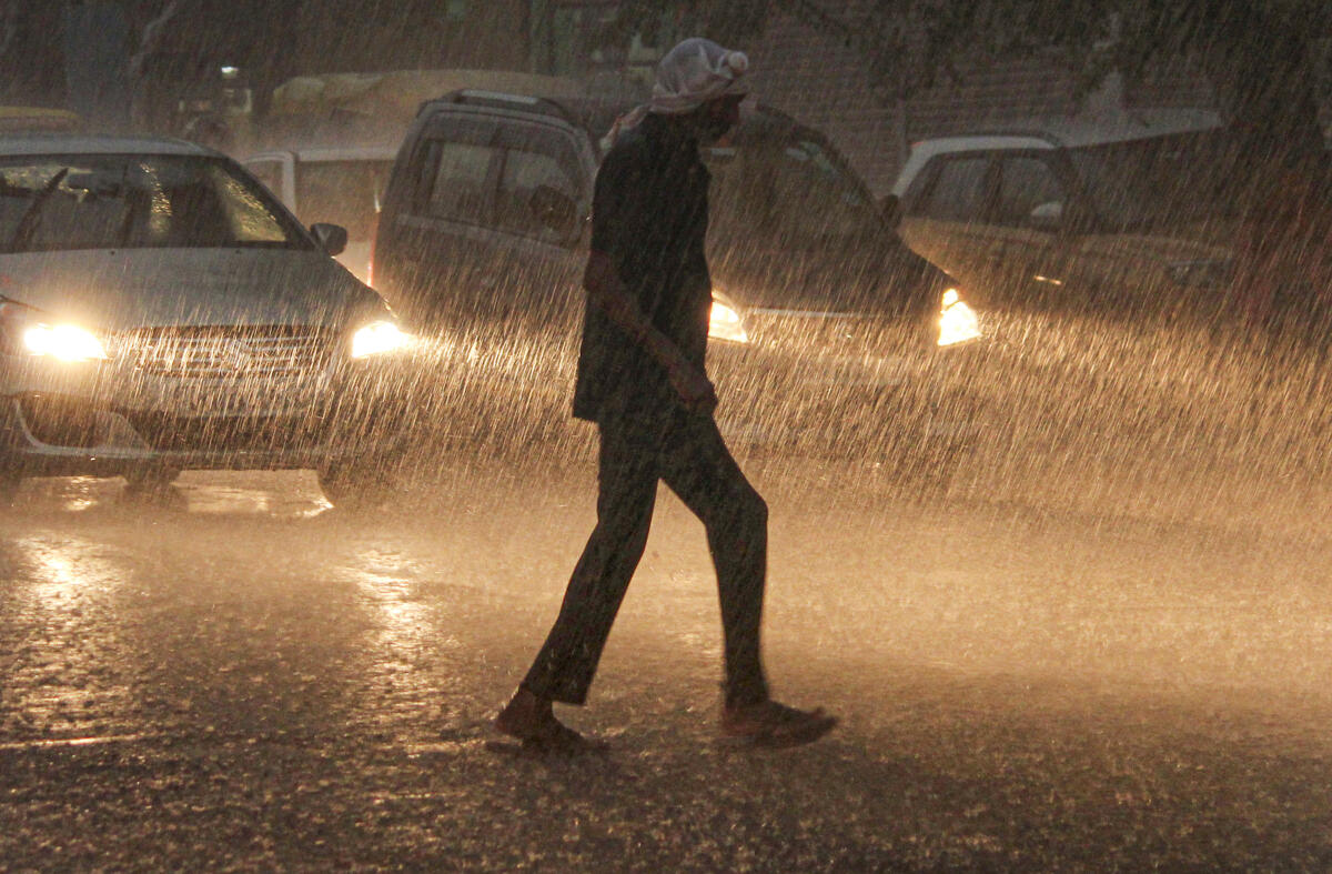 A man crosses a road amid rainfall, in Gurugram.