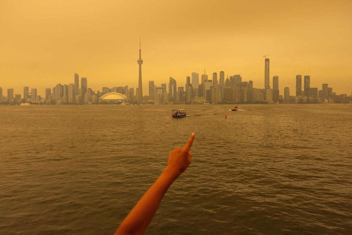 A person points to the skyline as they ride the ferry from Toronto Island as wildfire smoke from northwestern Ontario fills the sky, combined with an intense heat wave, prompting health warnings and calls for residents to limit outdoor activity in Toronto, Ontario, Canada.
