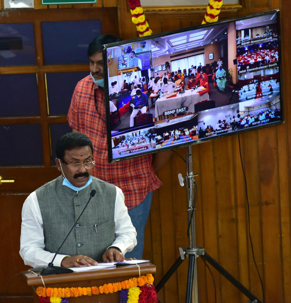 Taxation committee chairperson L Srinivas presents the BBMP budget. (R) Corporators, MLAs and MLCs follow the live-streaming at the zonal office, South Division, in NR Colony. DH photos/Irshad Mahammad & S K Dinesh