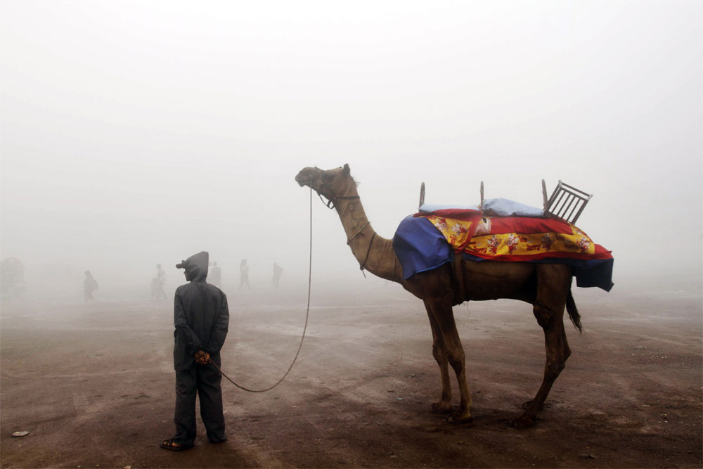 An Indian man waits with his camel for tourists to enjoy camel ride amidst mist during the monsoon festival at Saputara, about 420 kilometers (260 miles) south from Ahmedabad, India, Saturday, Aug. 4, 2012. The month long monsoon festival begins Aug....