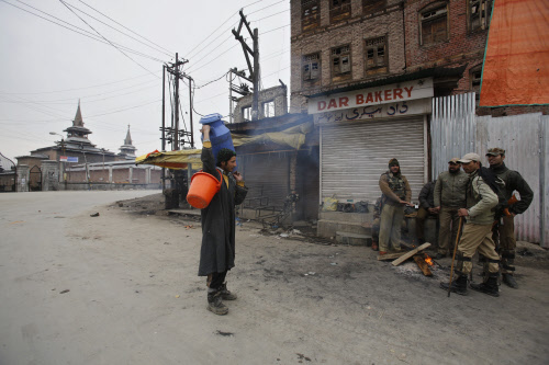 Government forces question a milk supplier as they warm themselves near a fire on a deserted street during a strike in Srinagar, India, Monday, Feb. 10, 2014. Authorities have imposed restrictions on movement of people in most parts of Indian-control...