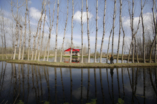 A Kashmiri man is reflected in a canal as he walks on the outskirts of Srinagar, AP Photo