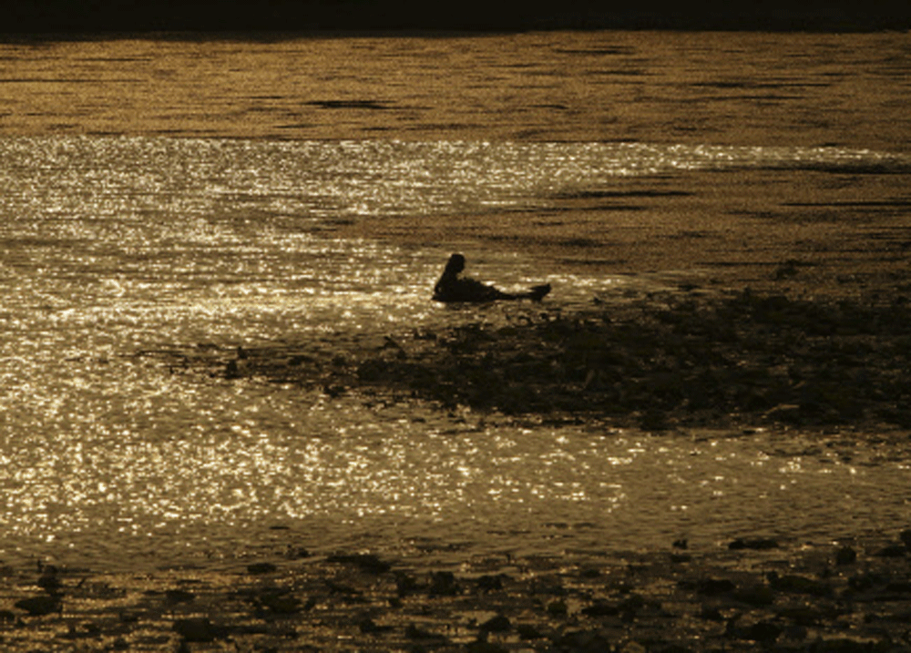 A man floats with the aid of an air filled tube as he returns after plucking Lotus flowers from Bindu Sagar Pond in Bhubaneswar, Monday, June 2, 2014, AP photo 
