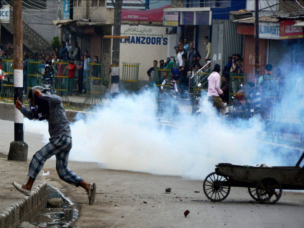 Youth run for cover amid tear gas smoke fired by the police during a clash at Saraf Kadal in Srinagar on Friday. PTI Photo.