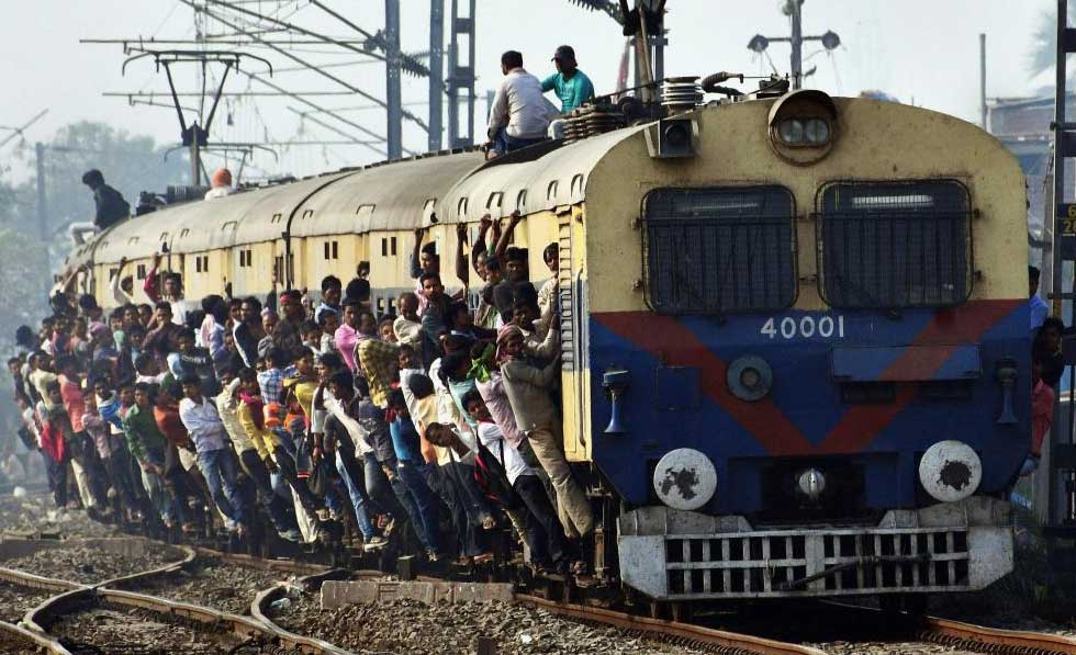 Passengers hang from the doors of an overcrowded train, in Patna on Wednesday. PTI Photo