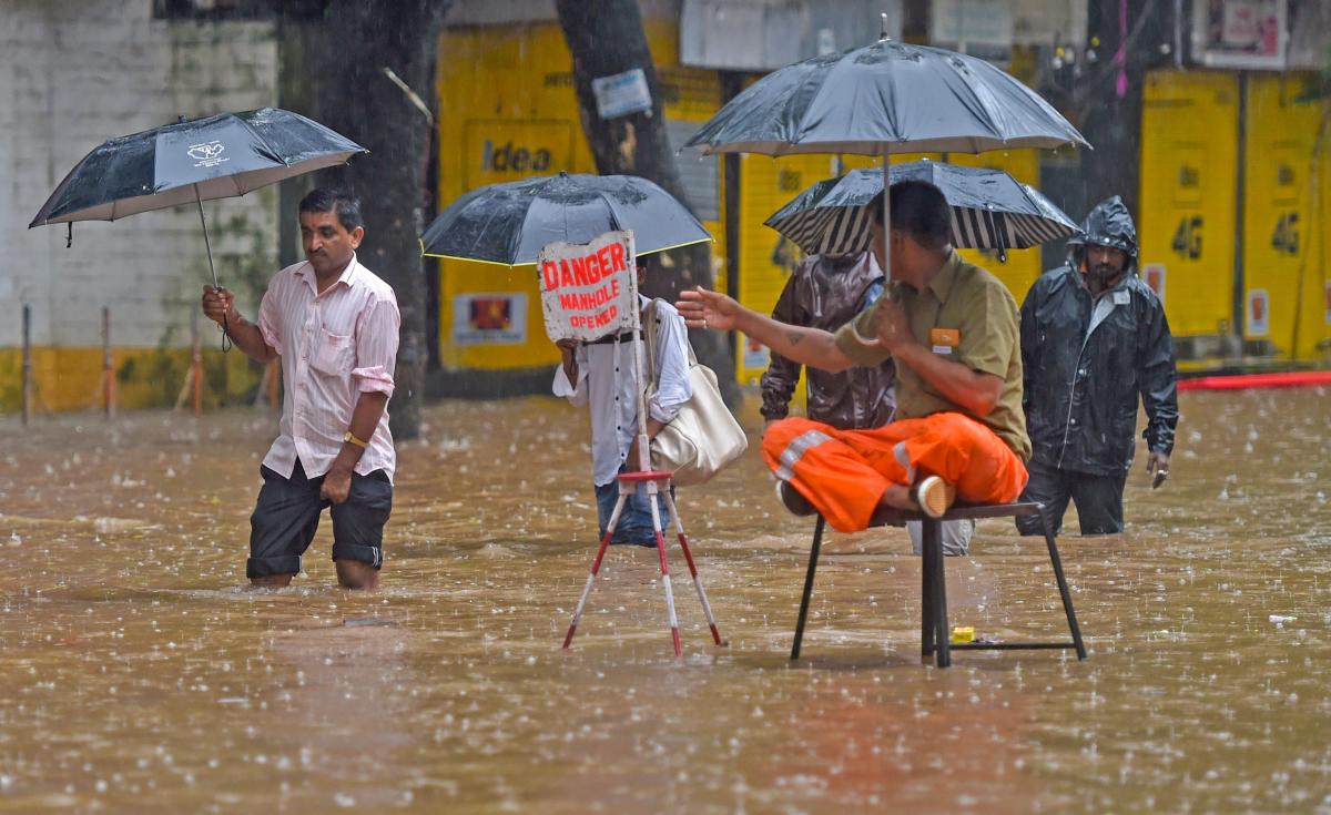 A municipal employee warns pedestrians about an open manhole as water floods the streets during heavy rainfall, in Mumbai on Tuesday, July 03, 2018. (PTI Photo)