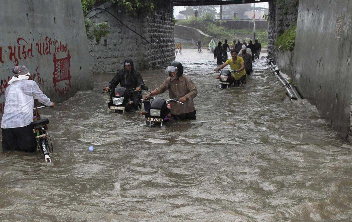 Commuters wade through a water-logged street after heavy rainfall, in Surat on Thursday, July 12, 2018. (PTI Photo)